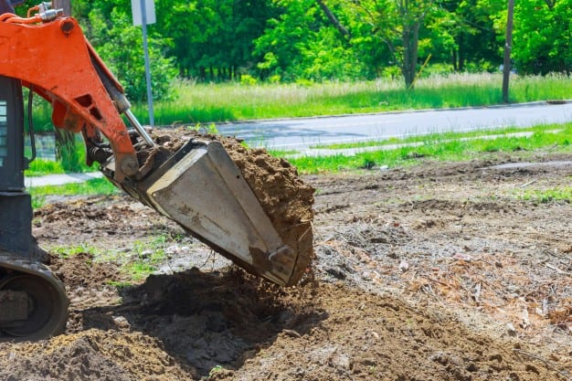 Excavator digging soil near road in sunny weather